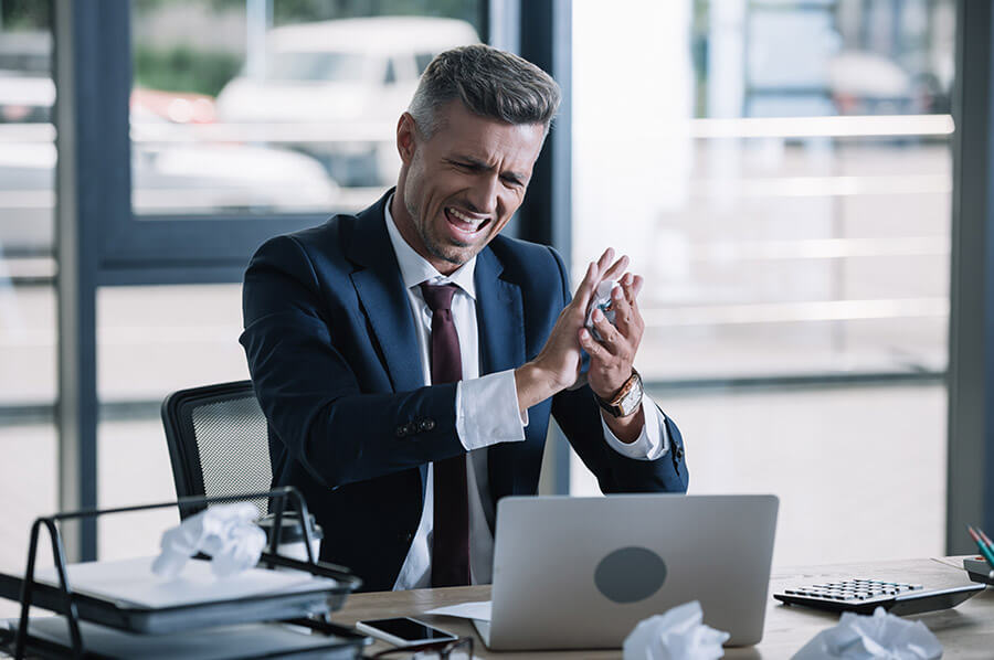 Frustrated businessman crumpling paper near laptop